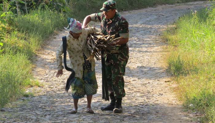 Salah satu anggota satgas TMMD di Desa Bodag, Kecamatan Kare, Kabupaten Madiun, Kapten Inf Agus Eko saat membantu seorang nenek mengangkat kayu bakar (29/7/2018)